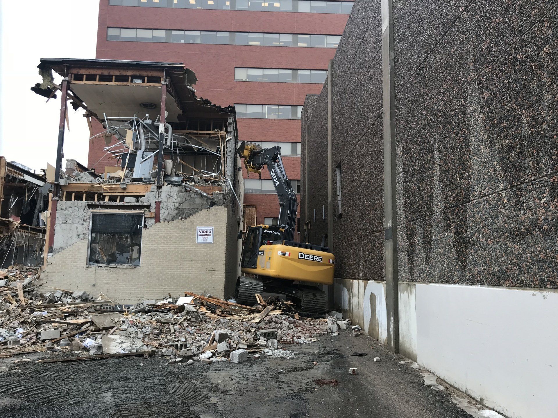 A large building is being demolished by a yellow excavator