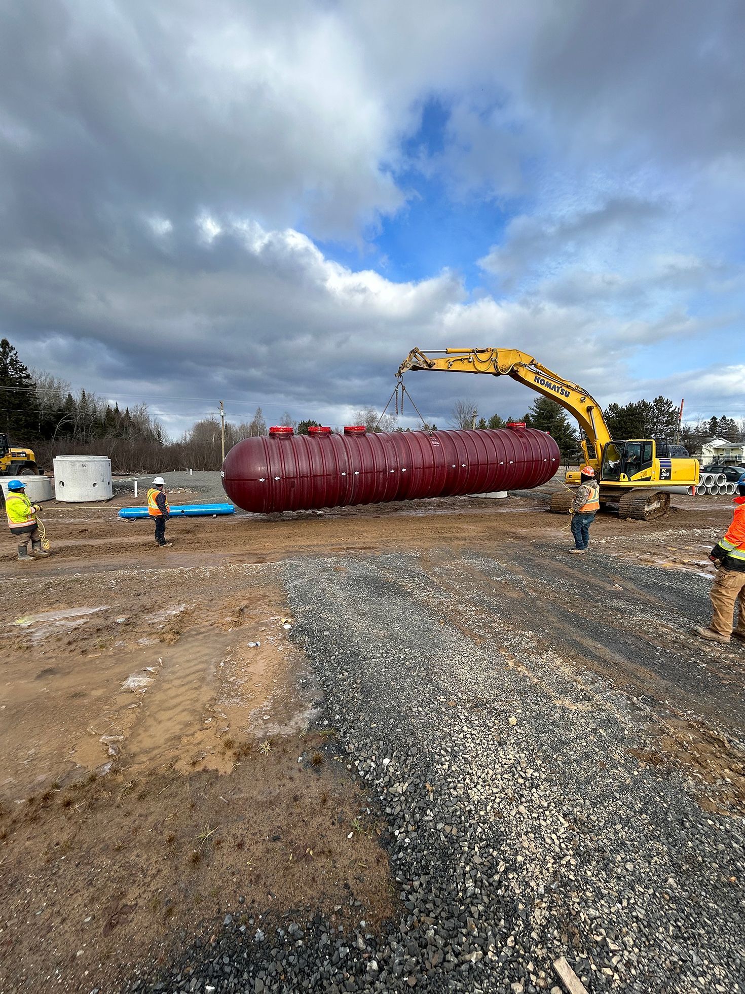 A large red tank is being lifted by a crane on a construction site.