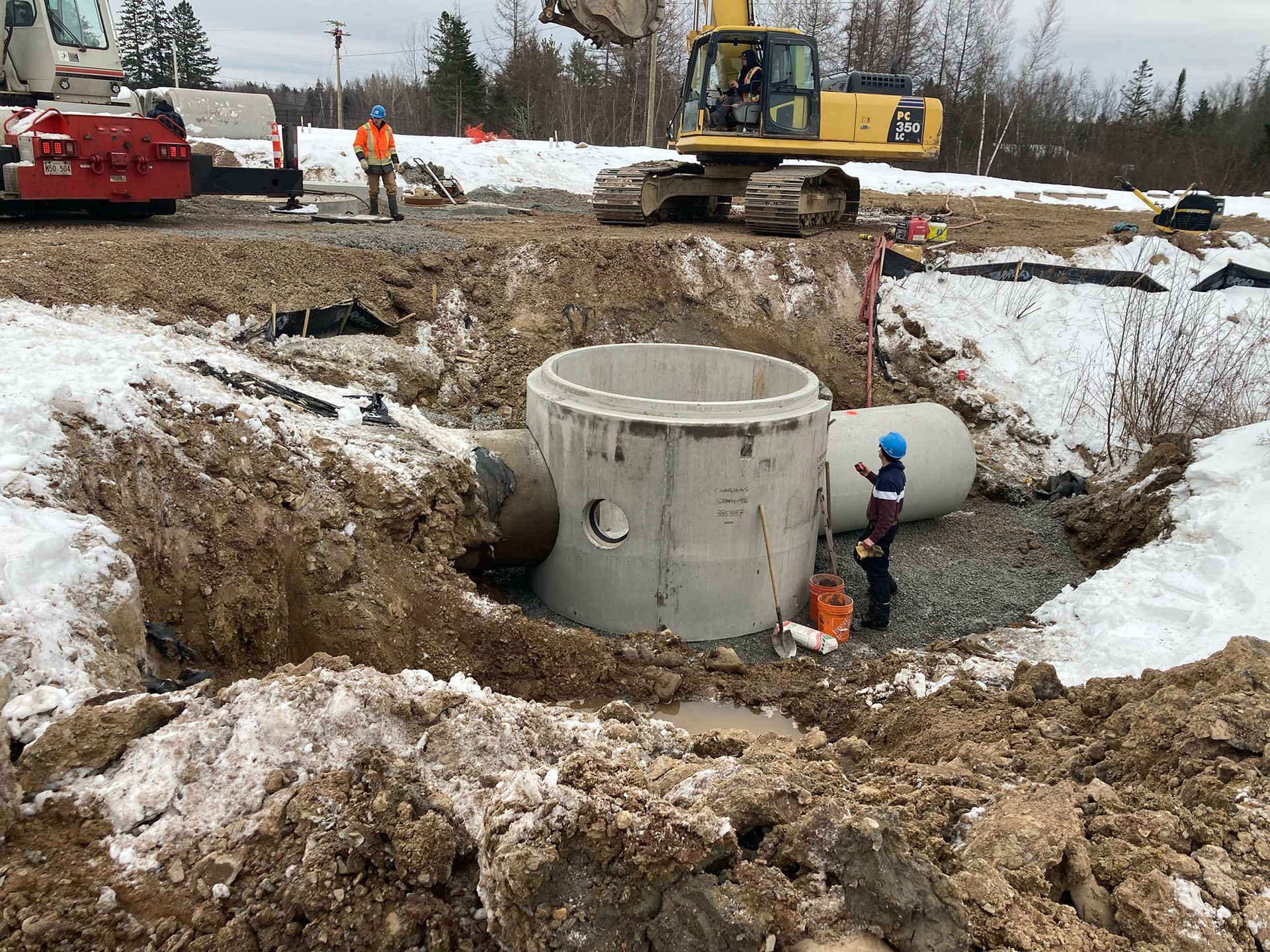 A man is standing in the dirt next to a large concrete pipe.