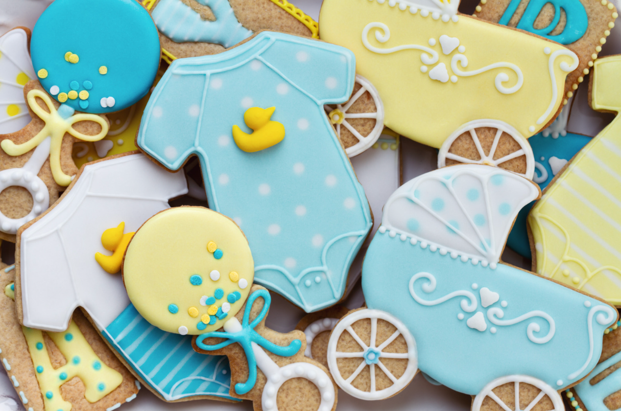 Baby-themed sugar cookies in blue and yellow. Onesie, rattle, stroller, and balloon designs.