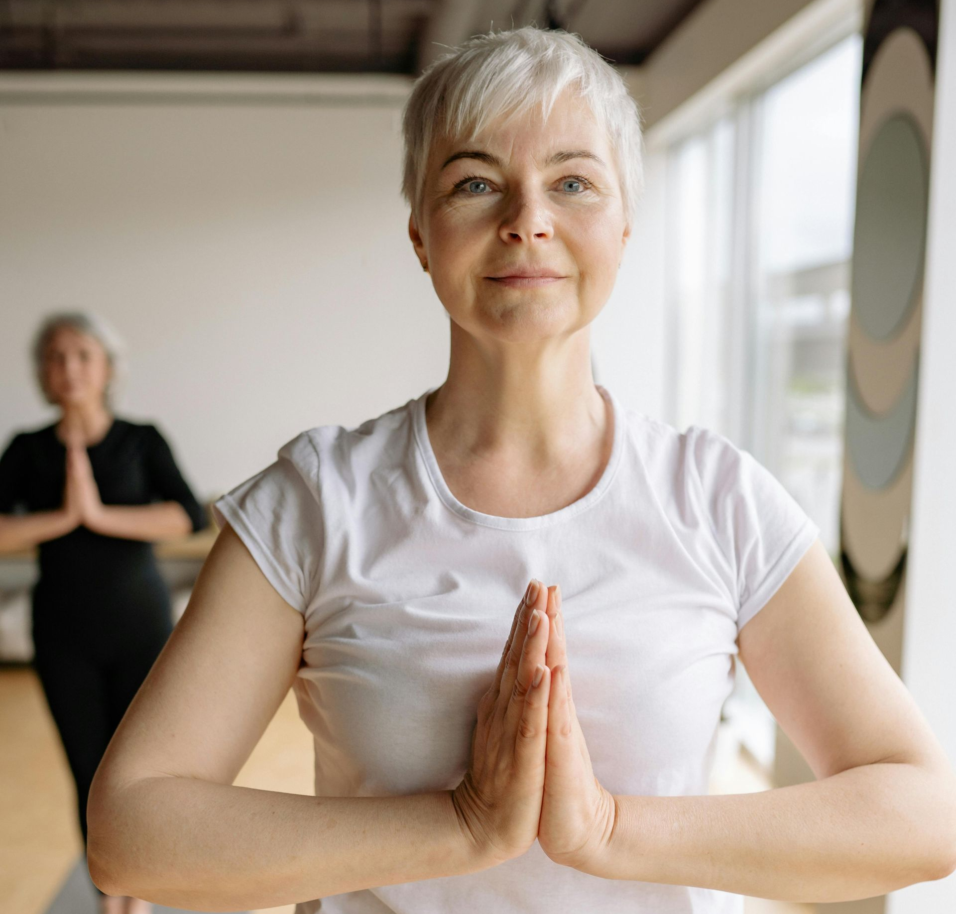 Person in a black long-sleeved shirt standing outdoors against a blue sky, arms raised with palms pressed together.