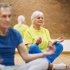 People sitting in a cross-legged meditation pose on mats in a room with a brick wall.