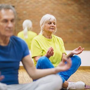 People sitting in a cross-legged meditation pose on mats in a room with a brick wall.