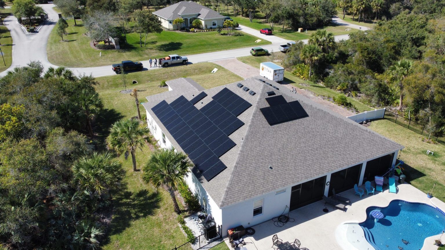 An aerial view of a house with solar panels on the roof and a pool.