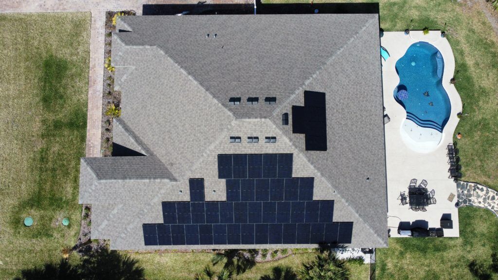 An aerial view of a house with solar panels on the roof and a pool.