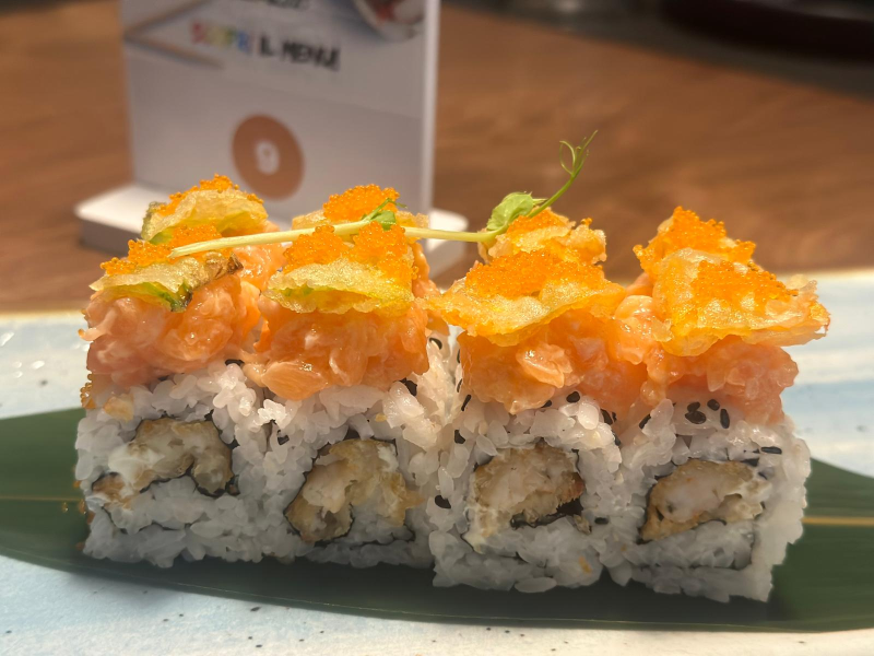 Rotolo di sushi con salmone, tempura croccante e uova di pesce su una foglia.