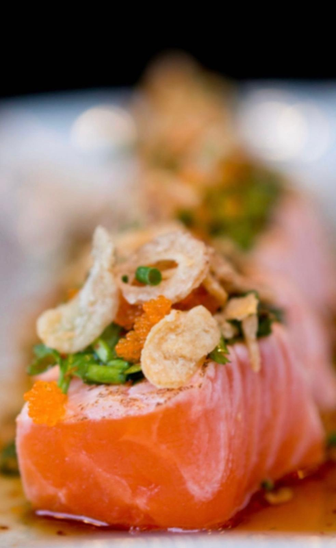 Sashimi di salmone condito con aglio fritto, cipollotti e uova di pesce.