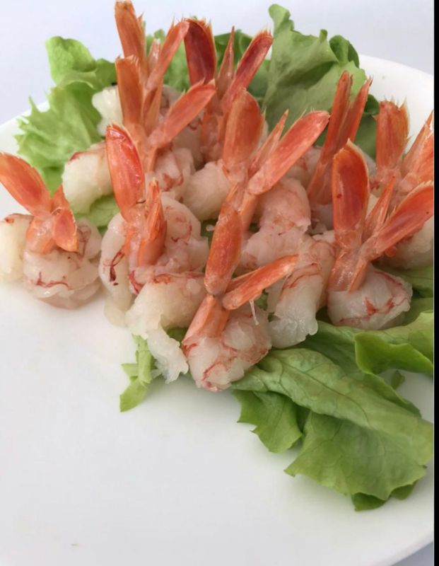 Gamberi cotti con la coda rosa su lattuga, piatto bianco.