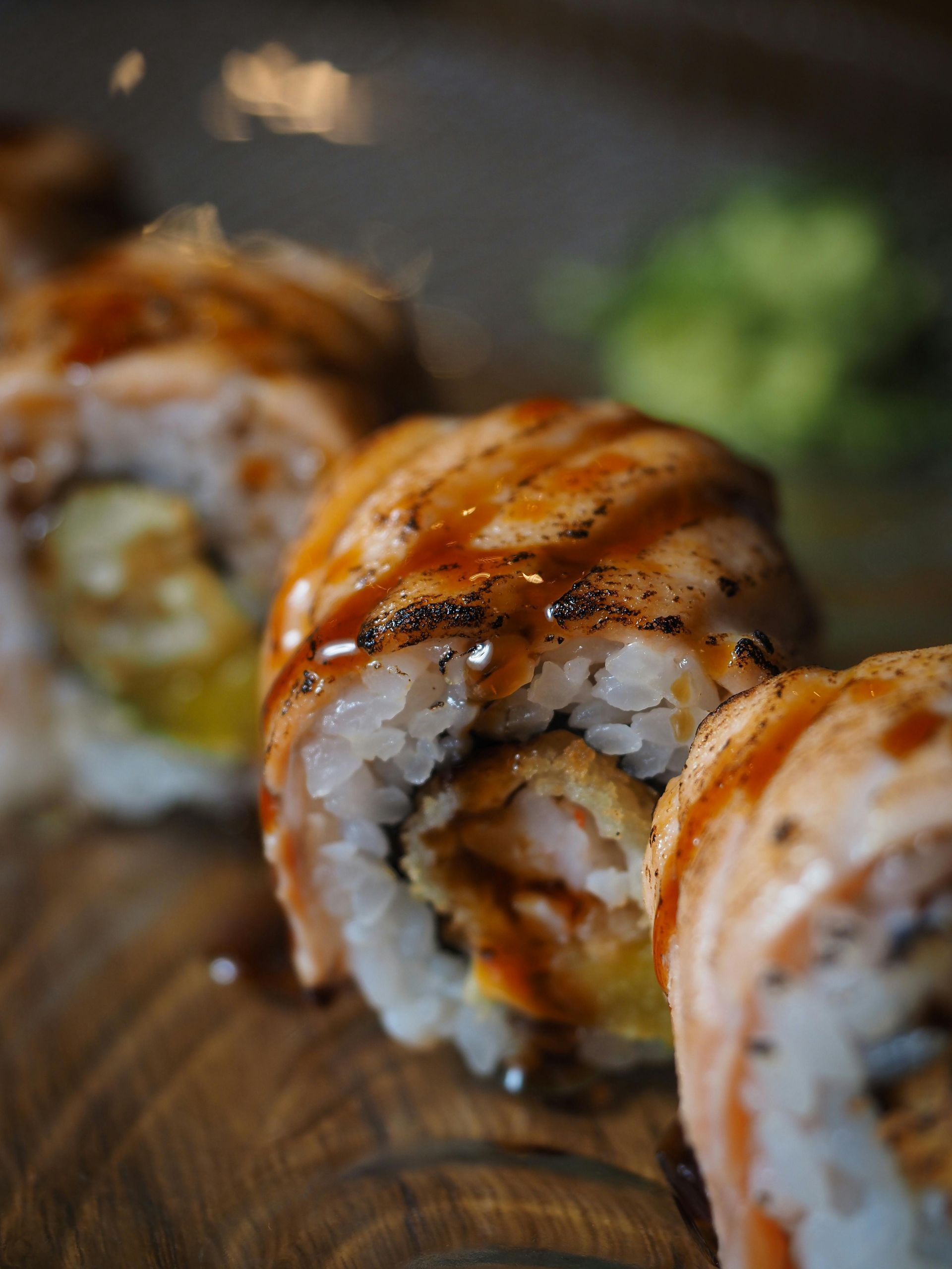 Rotolo di sushi con salmone, condito con salsa, su una superficie di legno, con un mucchietto di wasabi.