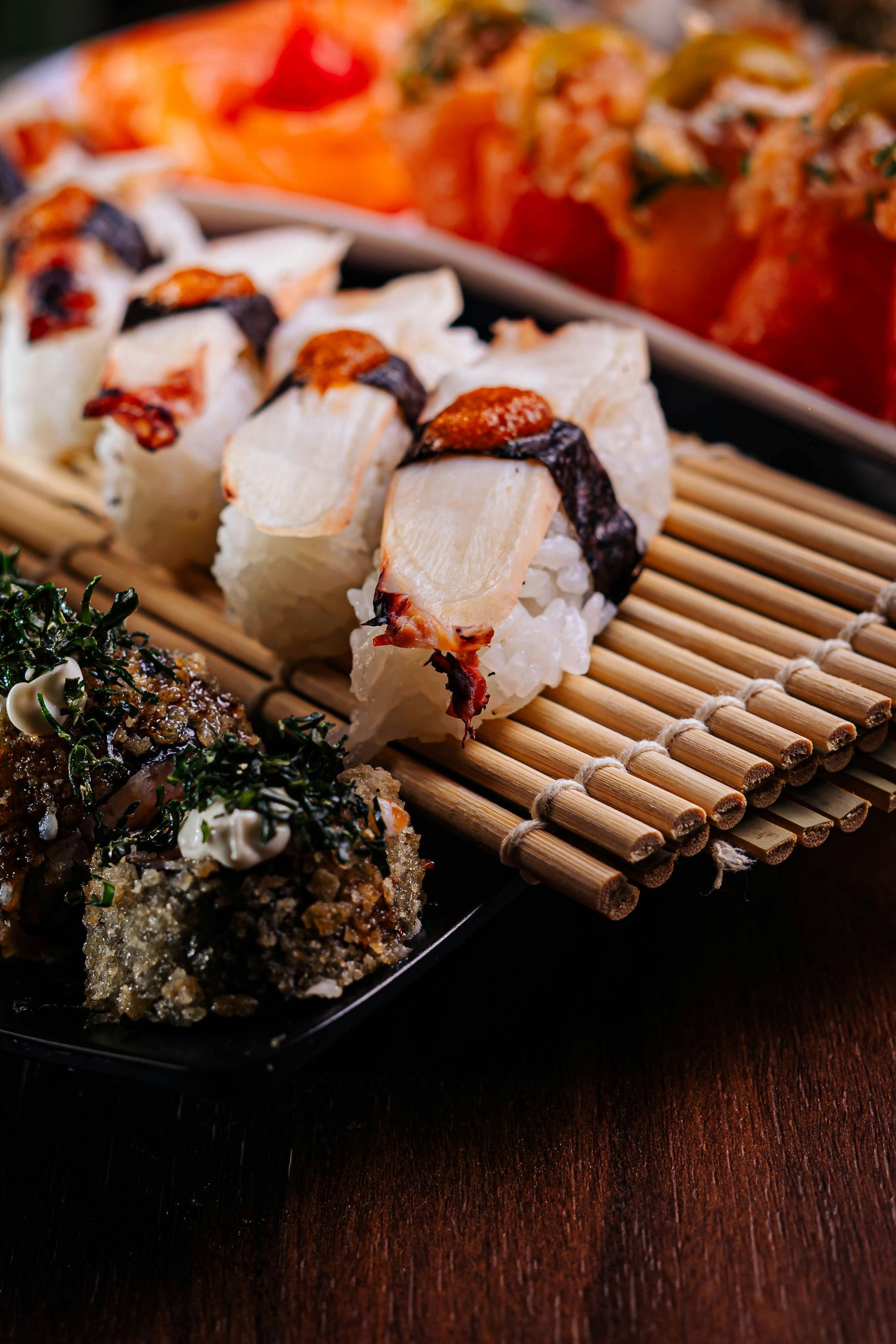 Piatto di sushi con nigiri e involtini su una stuoia di bambù, primo piano su un tavolo di legno scuro.
