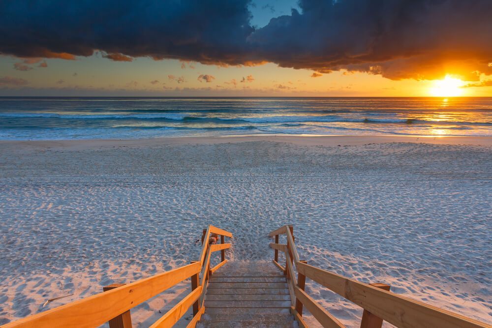 A Wooden Walkway Leading to The Beach at Sunset — Goldspark GC Electrical in Mermaid Beach, QLD