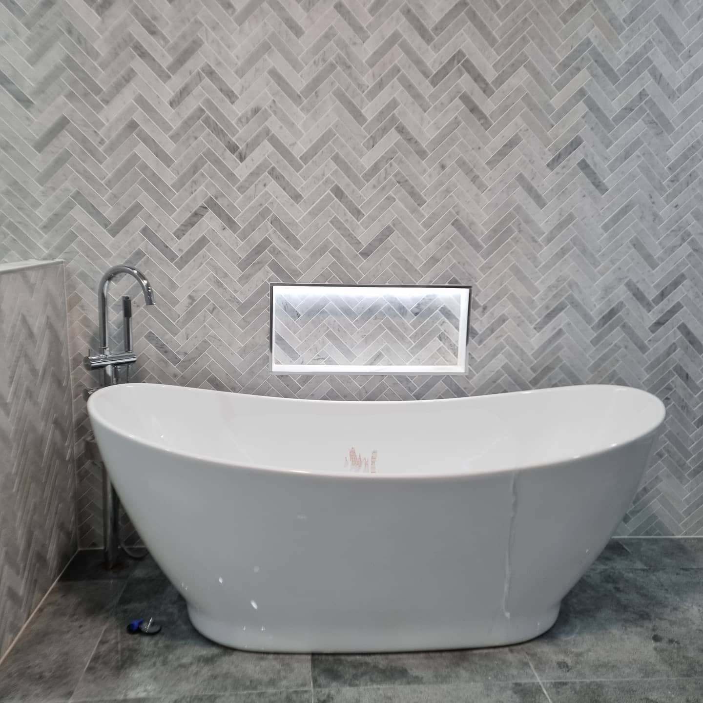 A White Bathtub Is Sitting in A Bathroom Next to A Wall with A Herringbone Pattern — Goldspark GC Electrical in Burleigh Waters, QLD