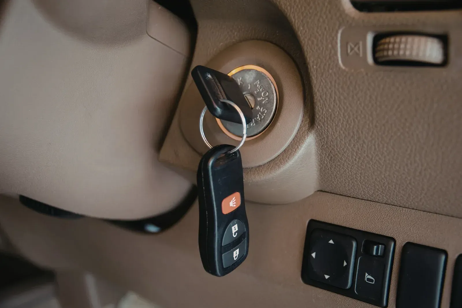 A car key is inserted into the ignition switch of a vehicle with a tan-colored interior dashboard.