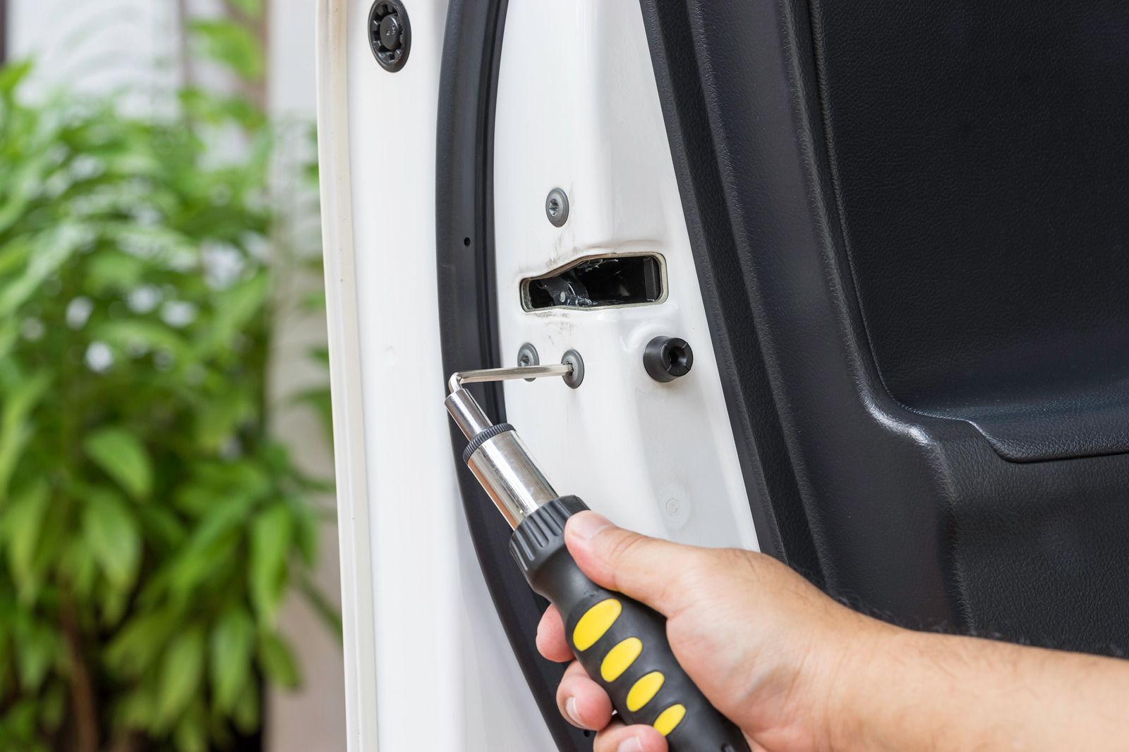A hand uses a screwdriver to tighten a screw on the edge of a white car door.