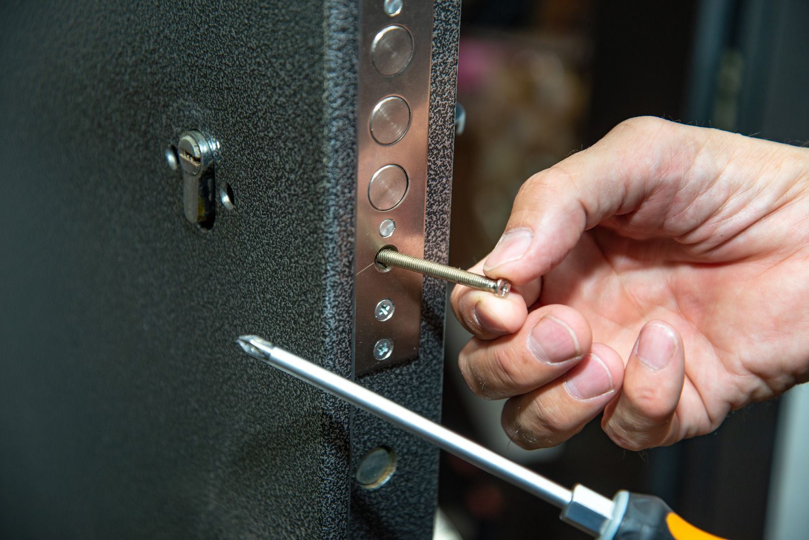 A close-up of a person using a screwdriver to install a long metal bolt into the side of a textured black door.