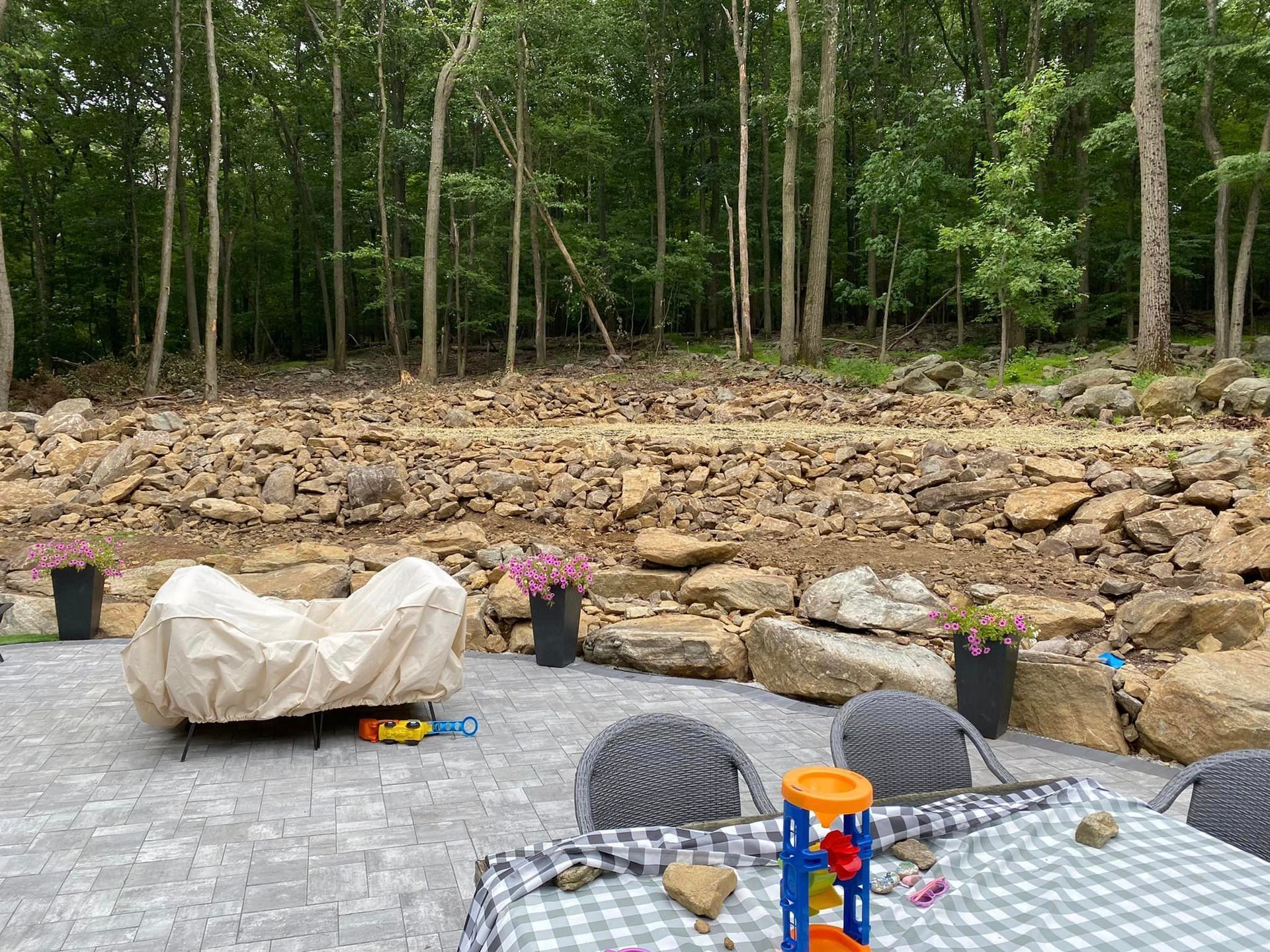 A table with a checkered tablecloth is sitting on a patio next to a pile of rocks.