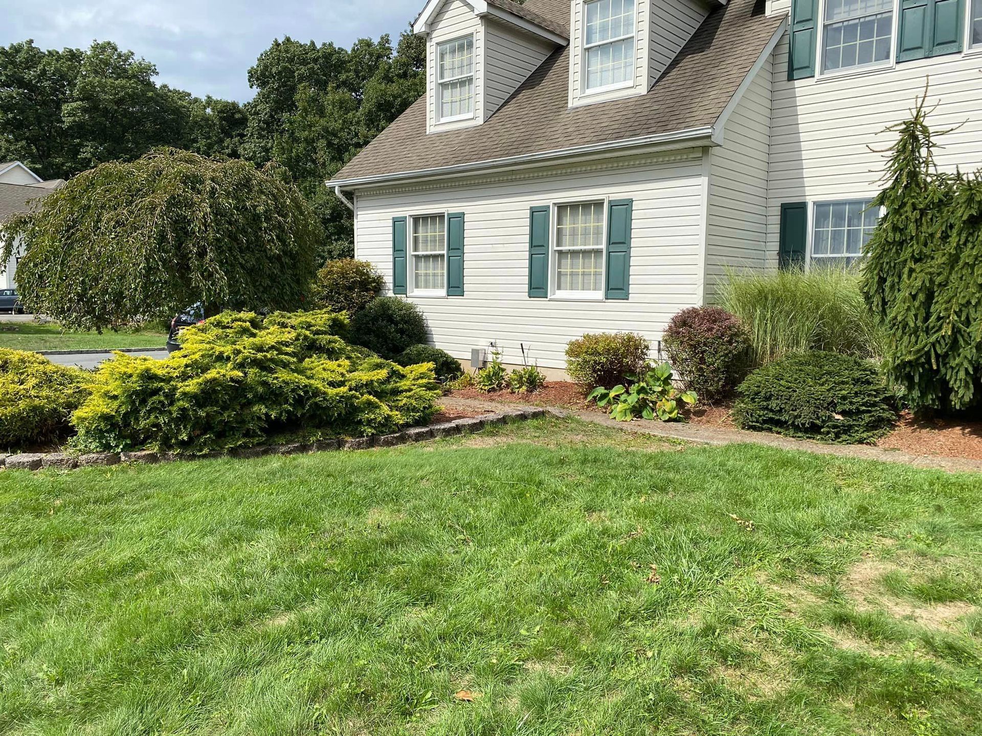 A white house with green shutters and a large lawn in front of it.