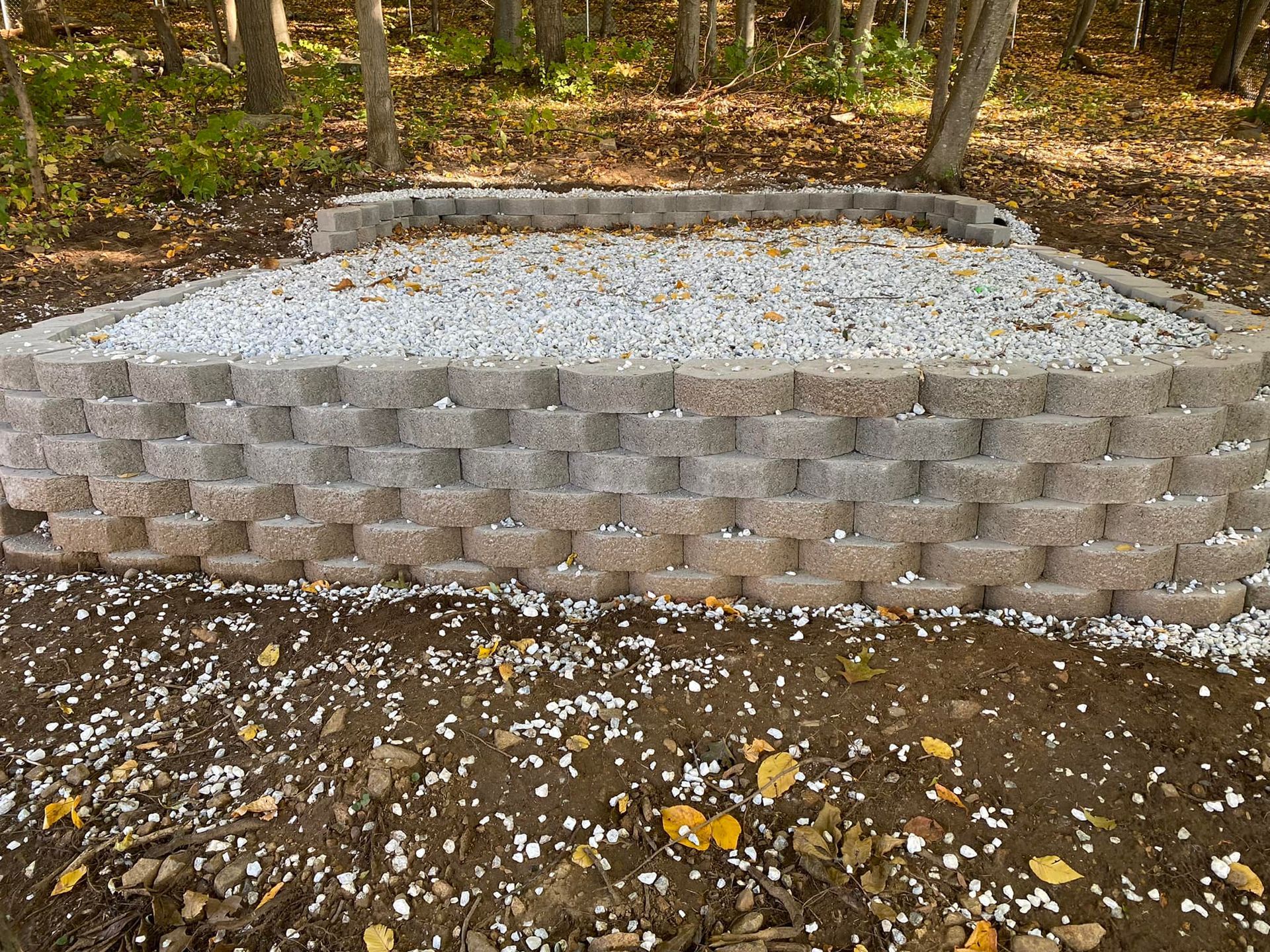 A brick wall is sitting on top of a pile of gravel in the middle of a forest.