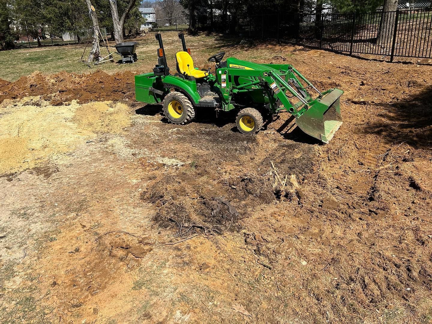A small green tractor is sitting in the middle of a dirt field.