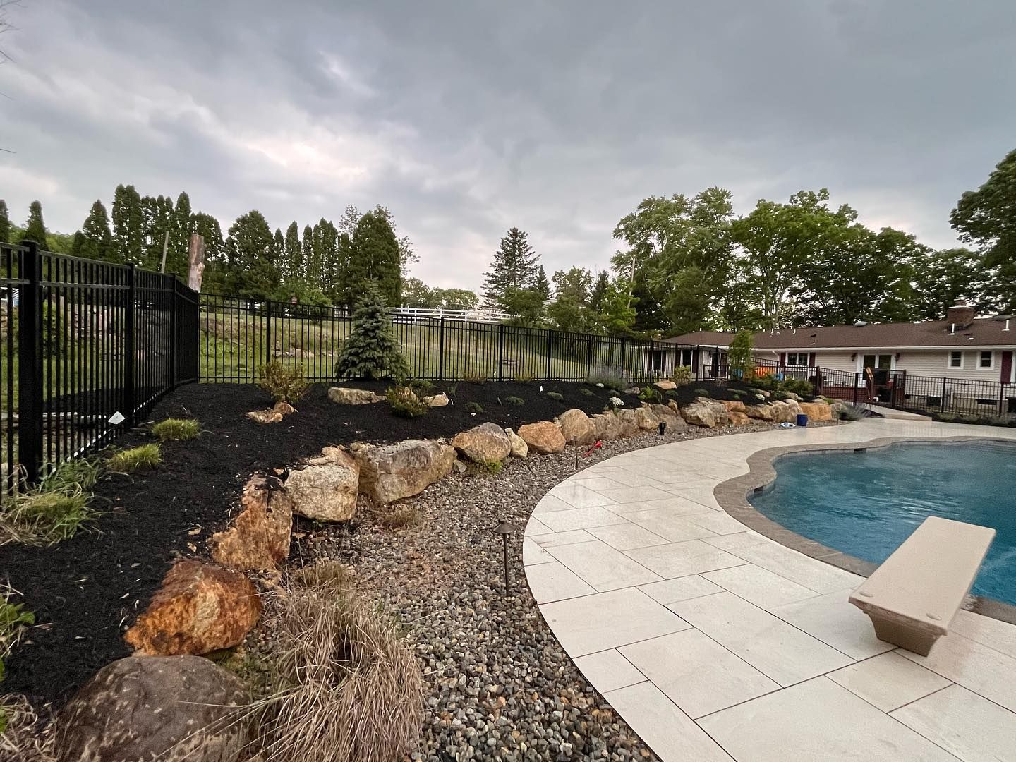 A large swimming pool is surrounded by rocks and a fence.
