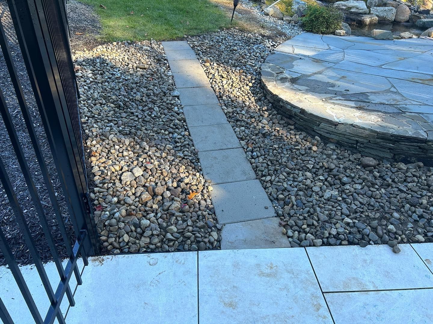 A stone walkway leading to a patio with a fence in the background.