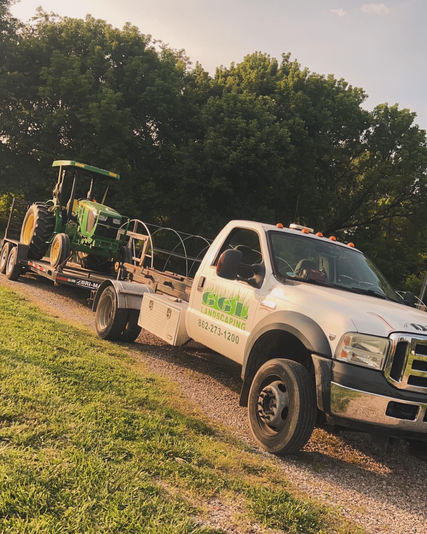 A white truck is towing a green tractor on a trailer.