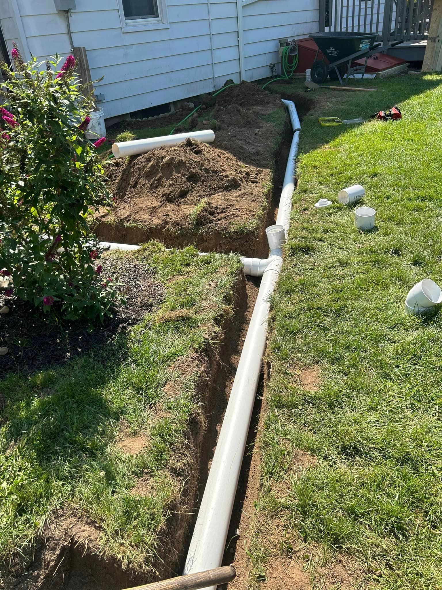 A drain pipe is being installed in a yard next to a house.