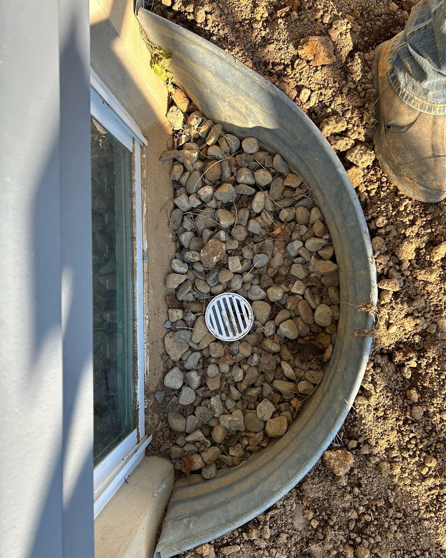 A drain hole in the ground next to a window.