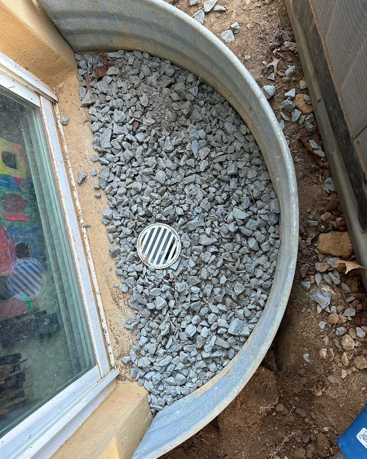A drain is sitting in a pile of gravel next to a window.