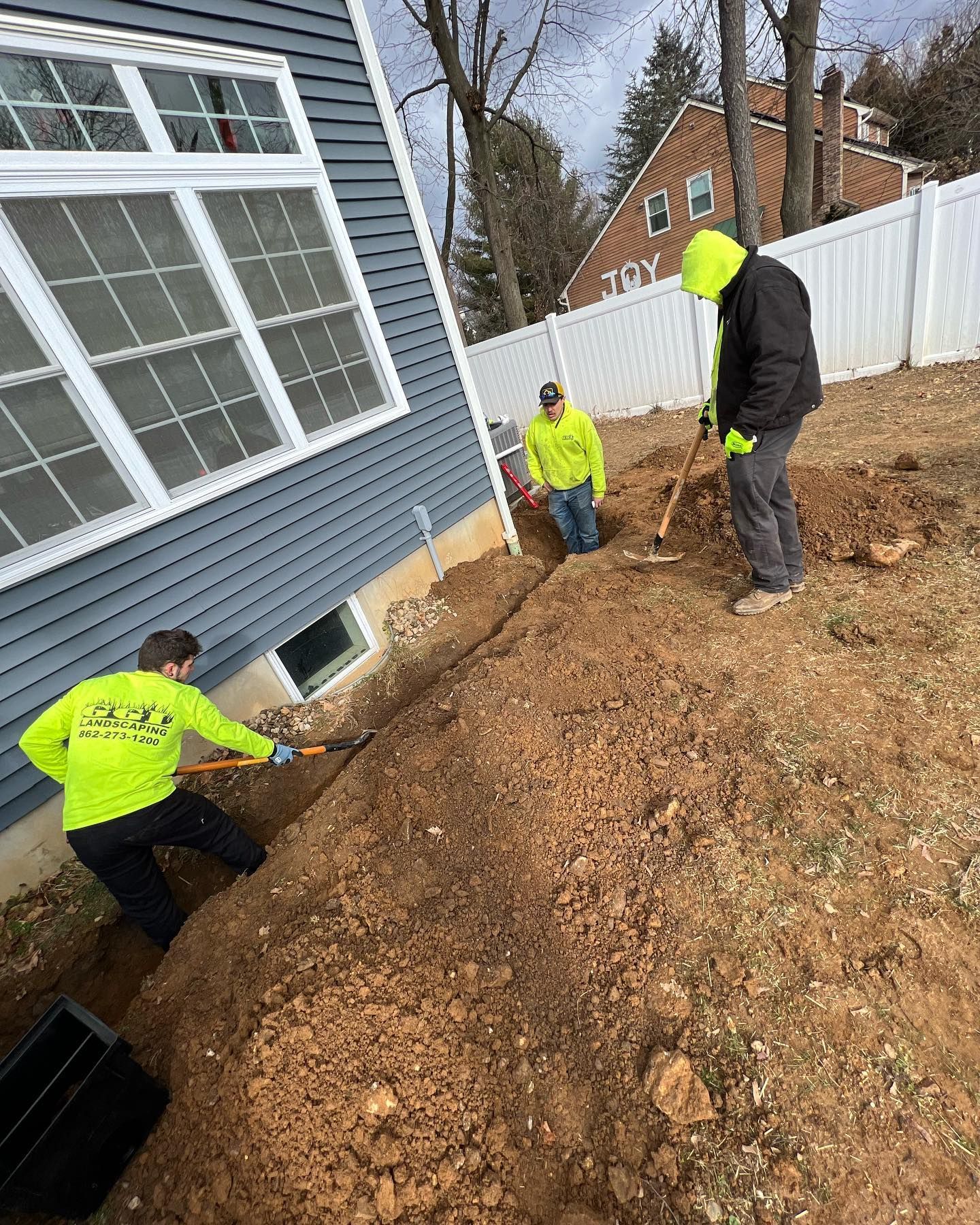 A group of people are digging in the dirt in front of a house.