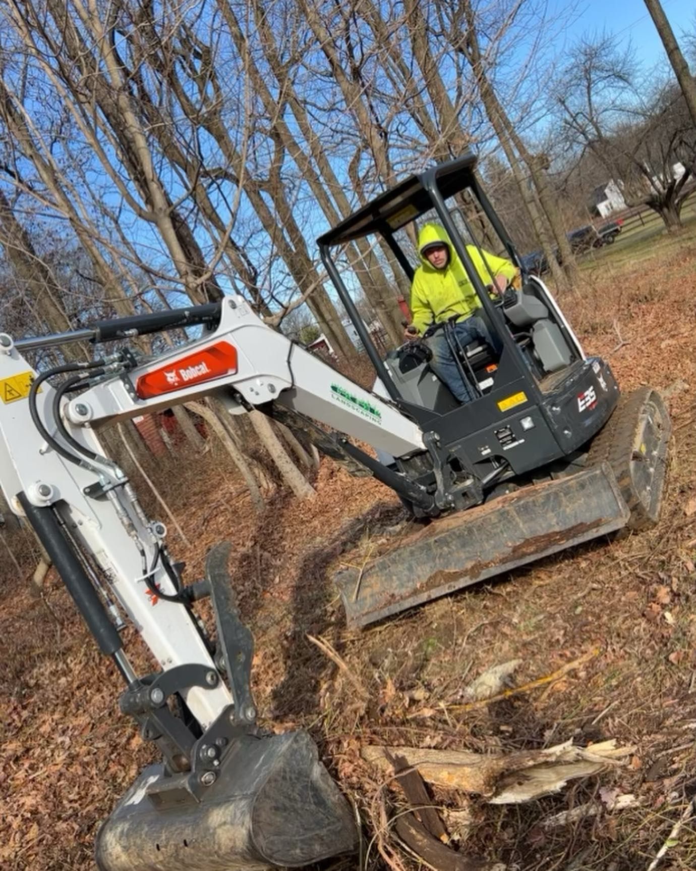 A man is driving a small excavator in the woods.