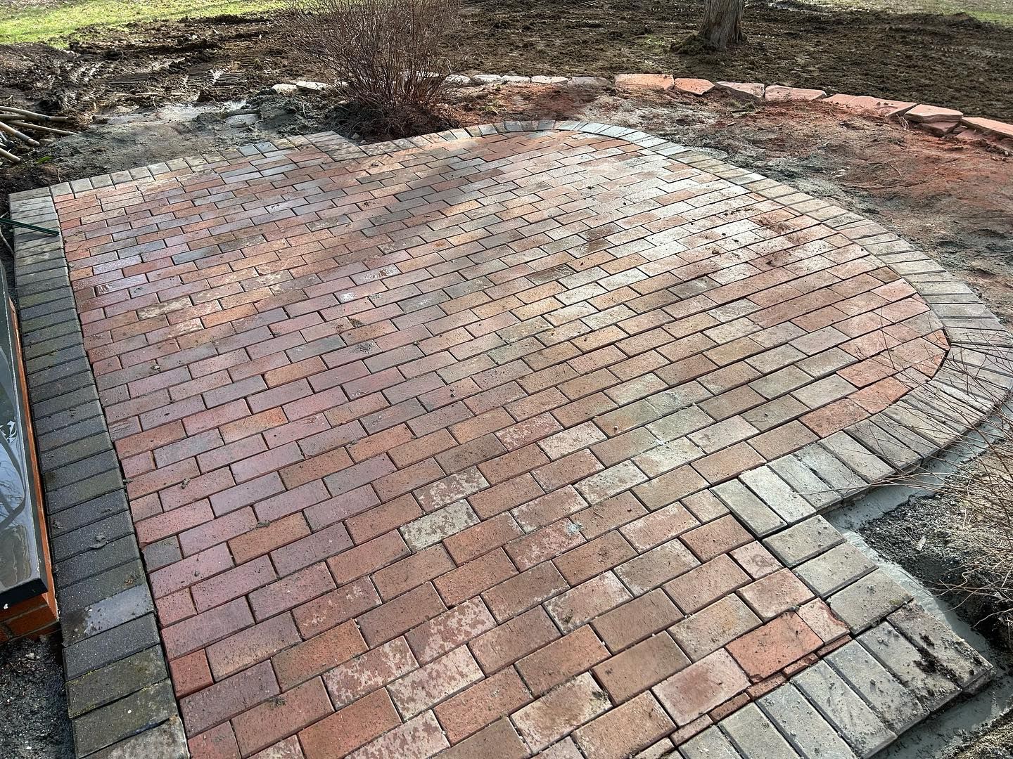 A brick patio is being built in a backyard.