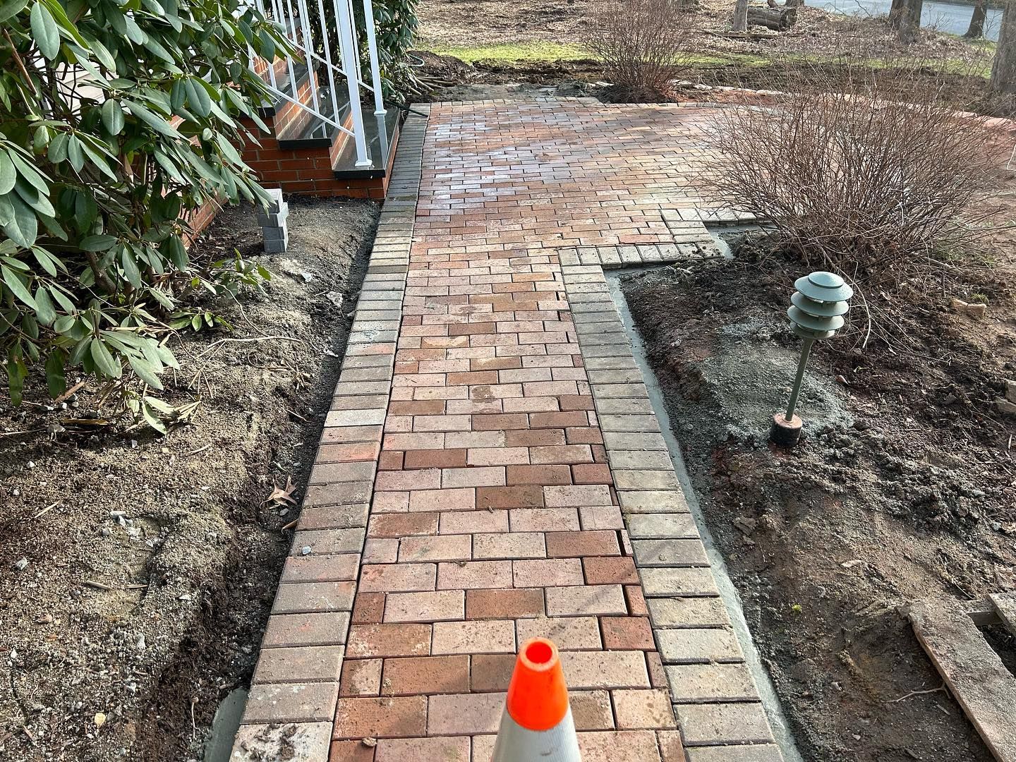 A brick walkway with a traffic cone on the side of it.