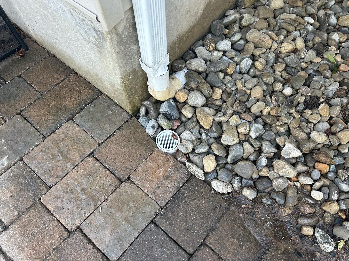 A drain on the side of a brick walkway next to a pile of rocks.