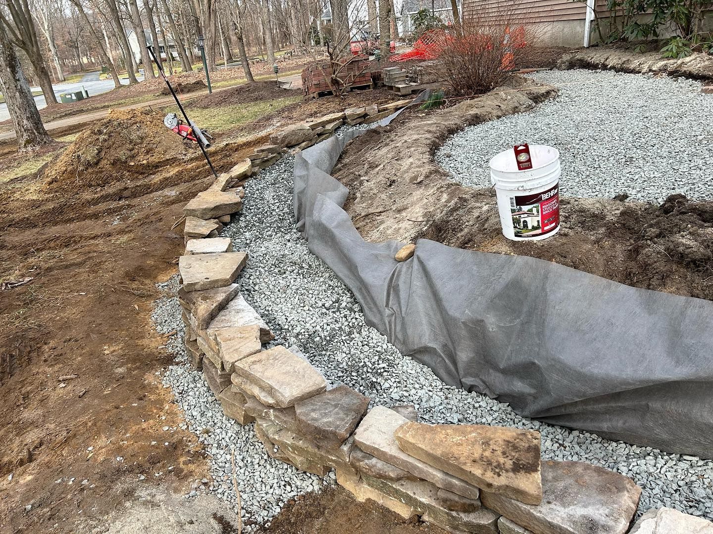 A bucket of gravel is sitting next to a stone wall.