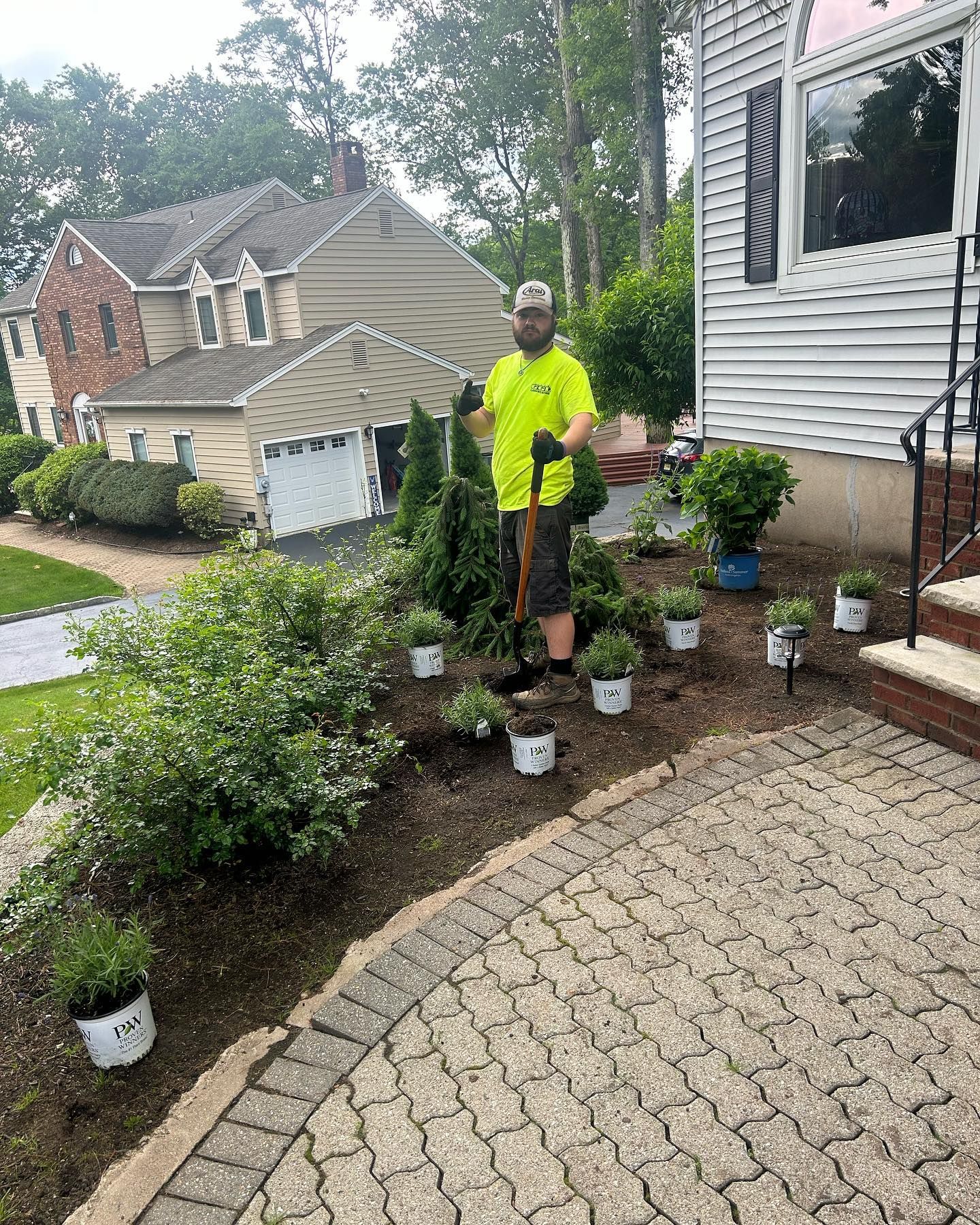 A man is standing in front of a house holding a shovel.