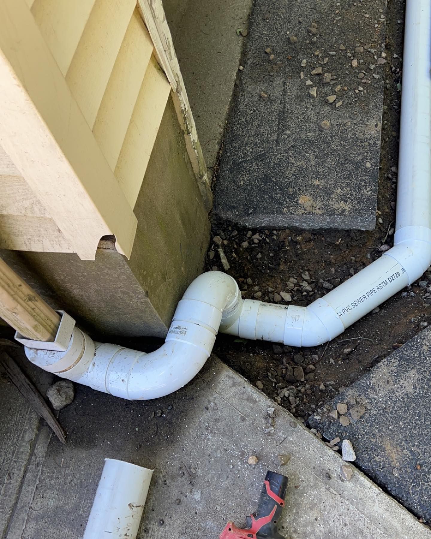A white pipe is connected to a wall next to a sidewalk.