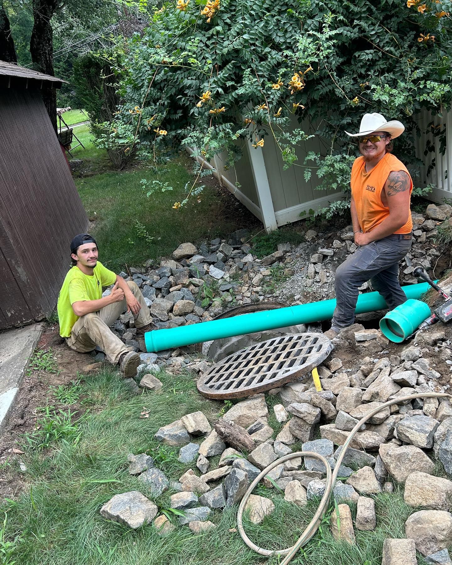 Two men are working on a drainage system in a backyard.