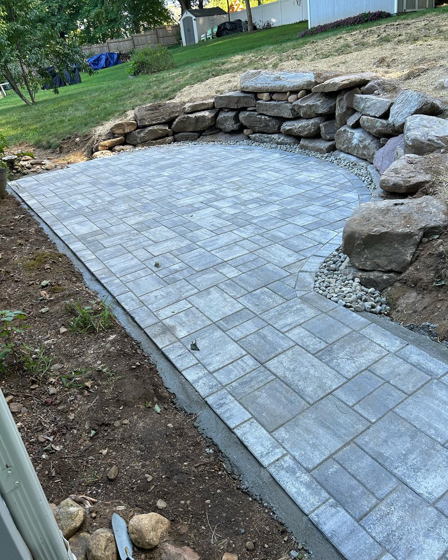 A brick walkway leading to a rock wall in a backyard.