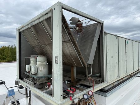 Large rooftop HVAC unit with angled metal fins, gauges, and electrical components.