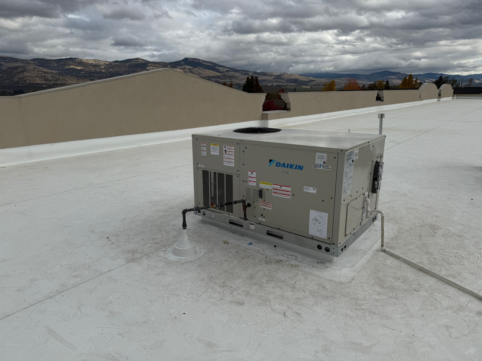 Rooftop HVAC unit on a white flat roof with a mountain backdrop under an overcast sky.