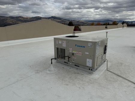 Rooftop HVAC unit on a white flat roof with a mountain backdrop under an overcast sky.