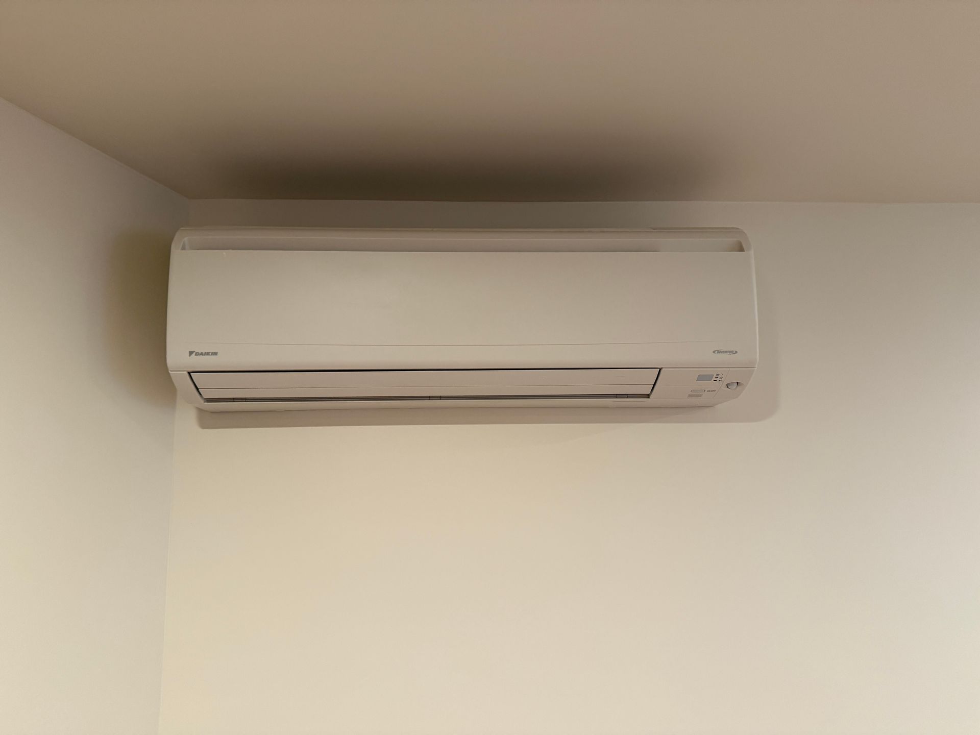 White wall-mounted air conditioner in a corner of a room, against a white wall.