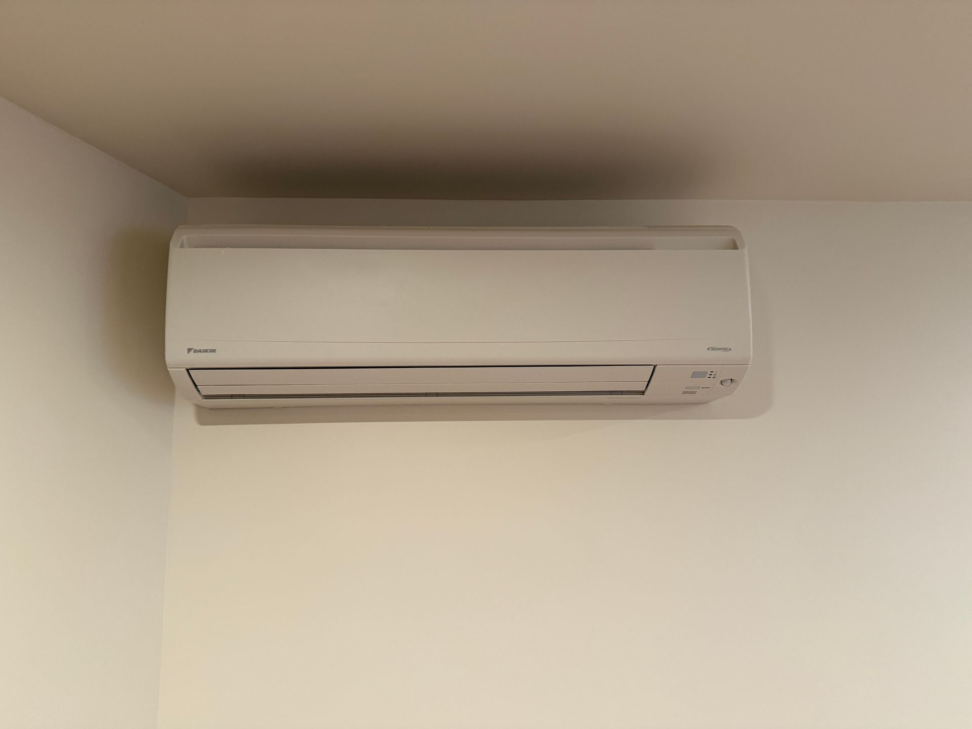 White wall-mounted air conditioning unit on a white wall in a corner.