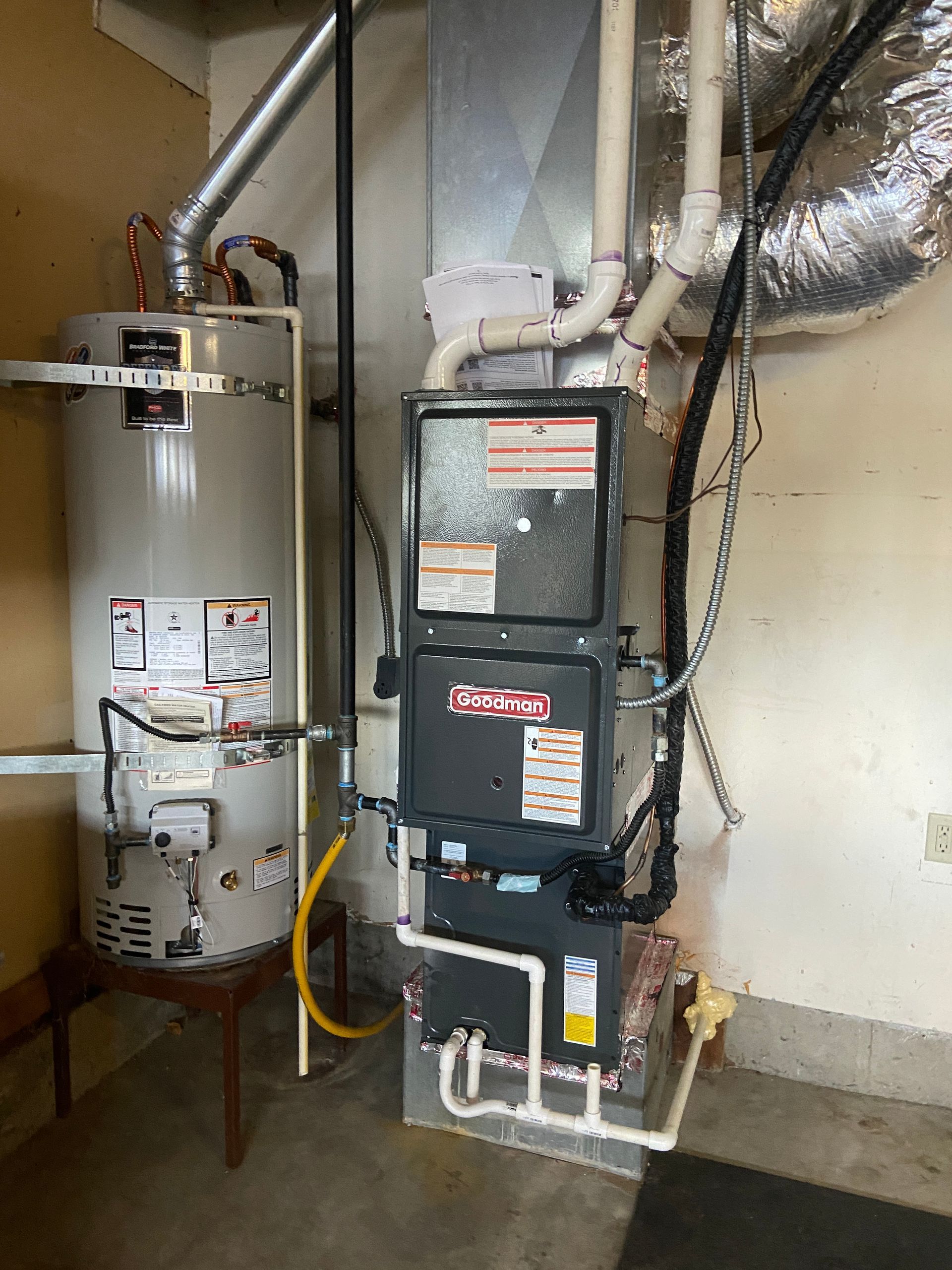 Water heater and furnace in a utility room; silver and gray appliances against a beige wall.
