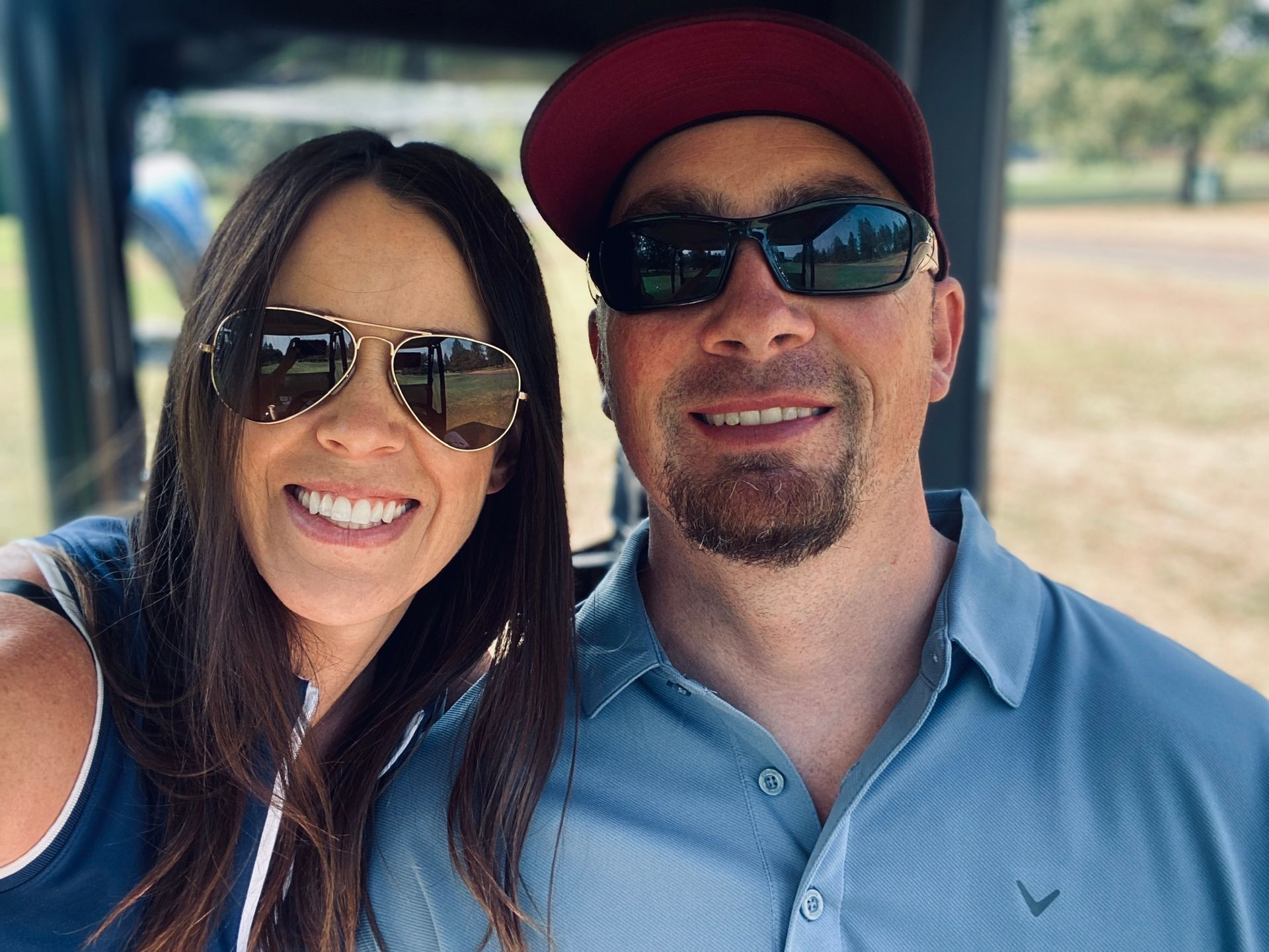 The owners of Trademark Tek in sunglasses smile at the camera while sitting in a golf cart.