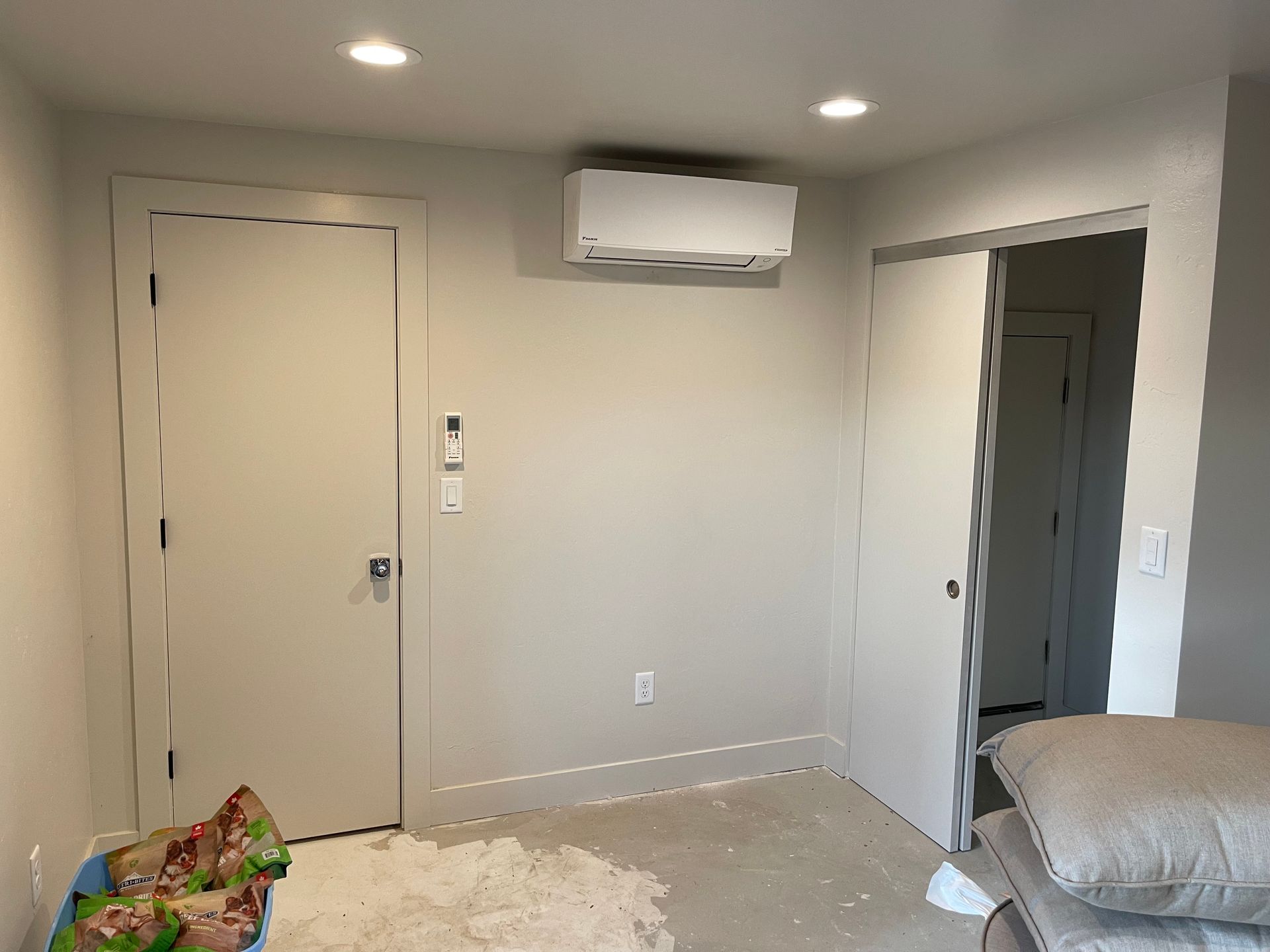 Interior room with closed doors, mini-split AC, unfinished floor, debris, and pillows.