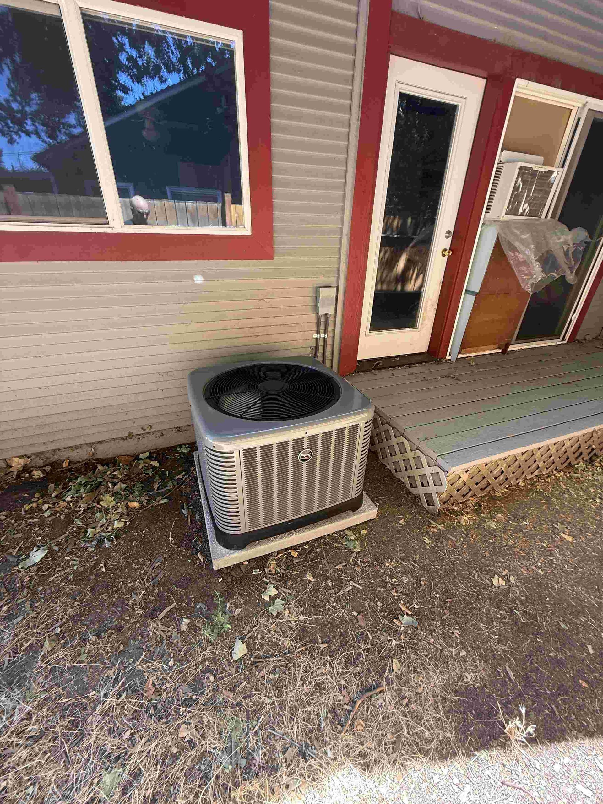 An air conditioning unit sits outside a building with a red frame window and door.