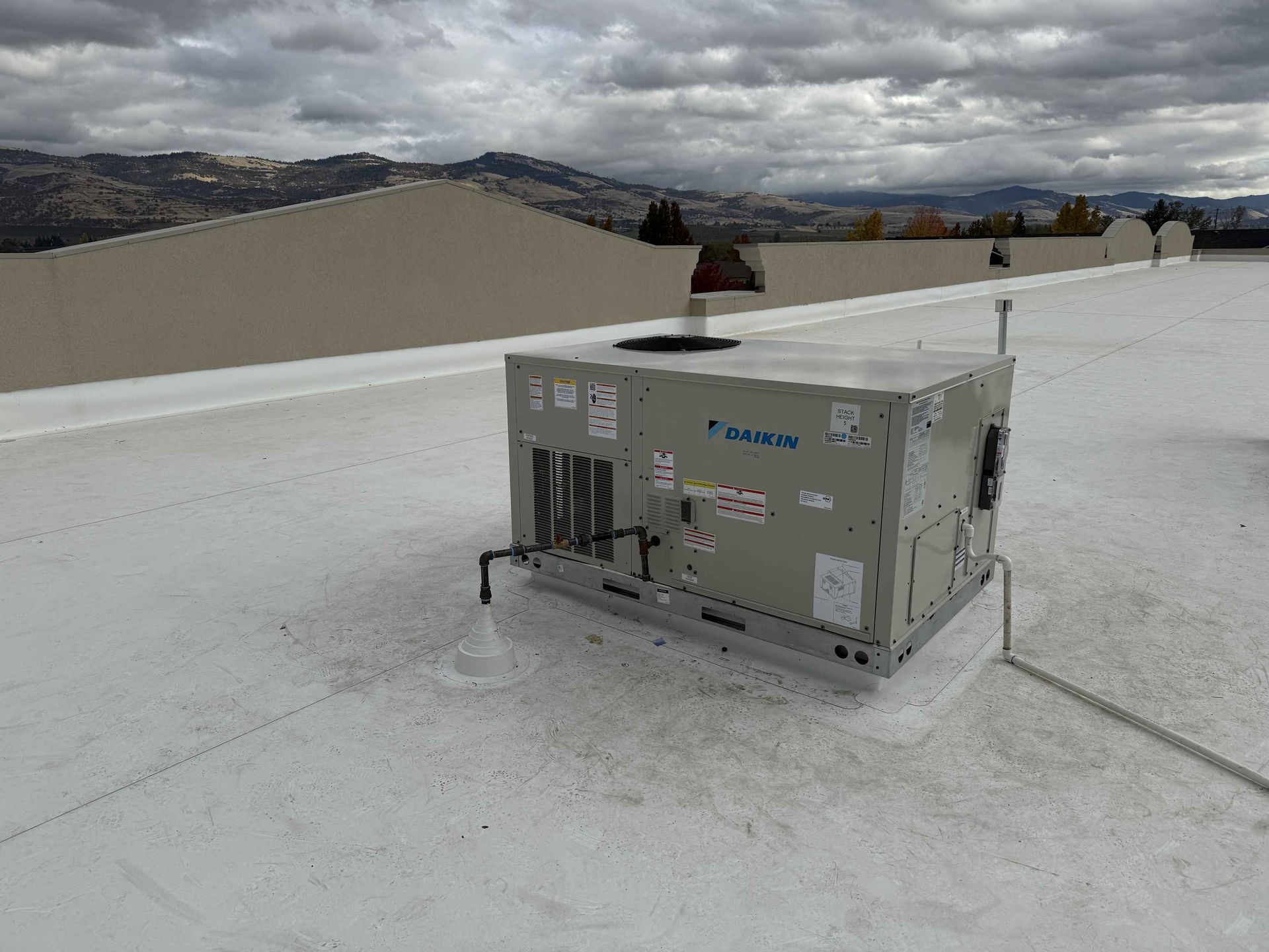 HVAC unit on a white rooftop with mountains in the background under a cloudy sky.
