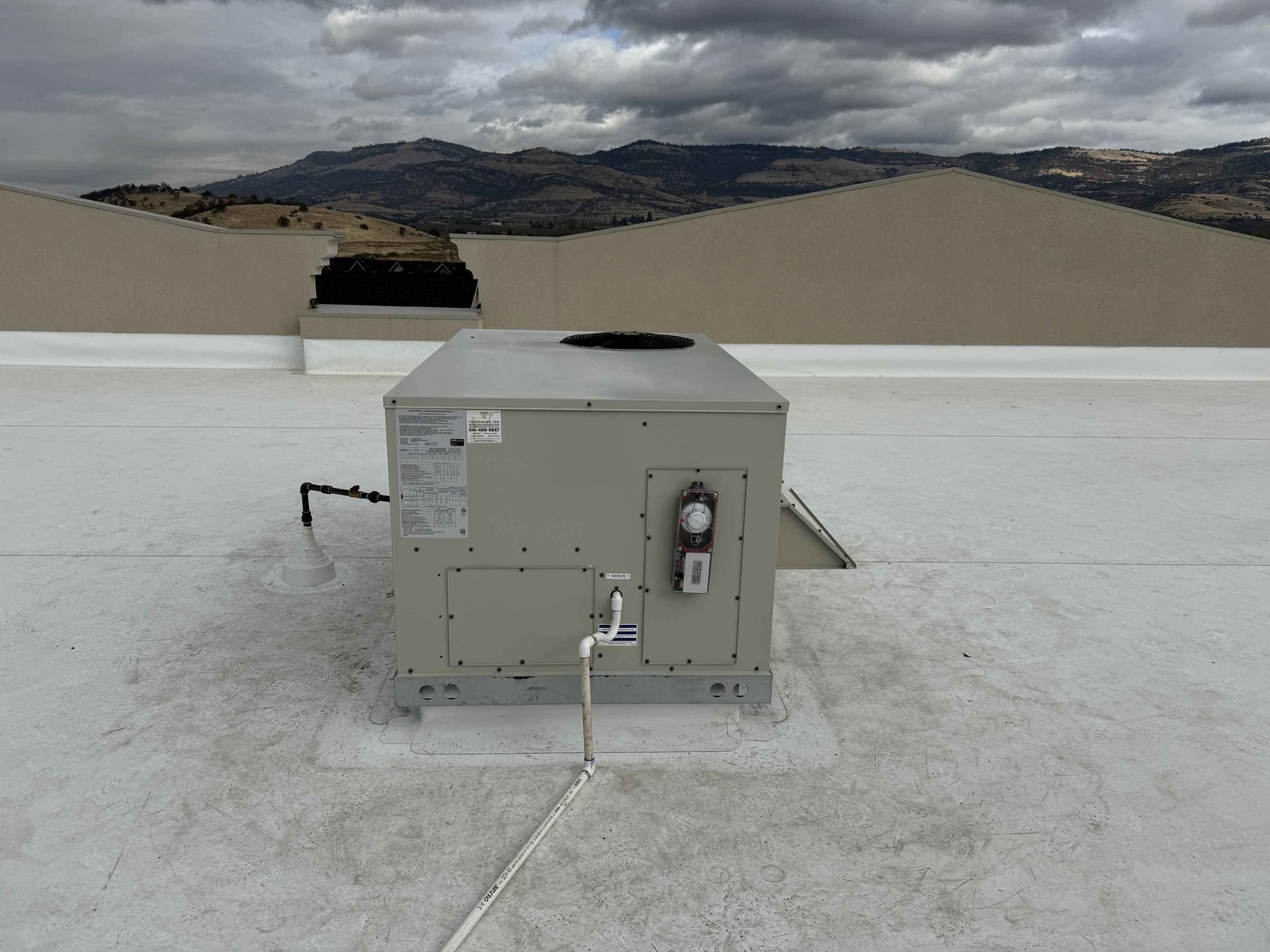 HVAC unit on a white roof with mountains in the background under a cloudy sky.